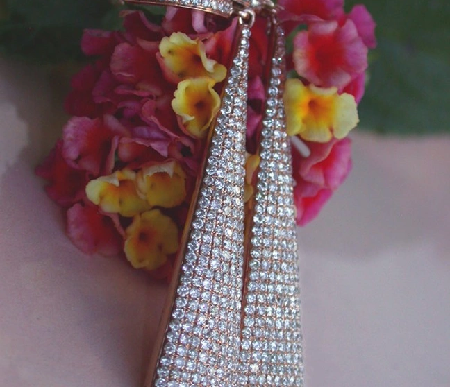 Interessante Diamanten-Ohrgehänge in Roségold, detailreich, vor Blüten im Sonnenlicht Interessante Diamanten-Ohrgehänge in Roségold, detailreich, vor Blüten im Sonnenlicht