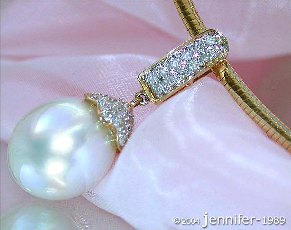 Goldener Anhänger mit Südseeperle und Brillanten, Detailaufnahme auf rosa Stoff.