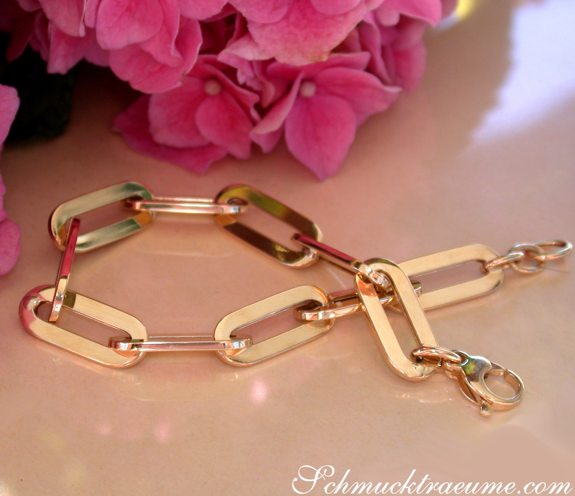 Gold-Paperclip-Armband in Gelbgold 585, minimalistisch, modern, Detailaufnahme, rosafarbene Blüten im Hintergrund