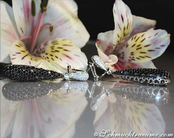 Schwarz-weiße Diamant-Ohrringe mit Edelsteinen, detailreich, vor Lilienblüten.