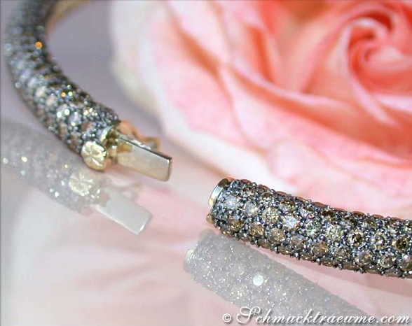 Glanzvolles Goldarmband mit braunen Brillanten, detailreiches Design, rosafarbene Blume im Hintergrund