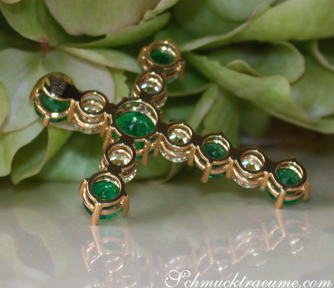 Goldener Kreuzanhänger mit Smaragden und Brillanten, detailreich, auf grünen Blättern liegend.