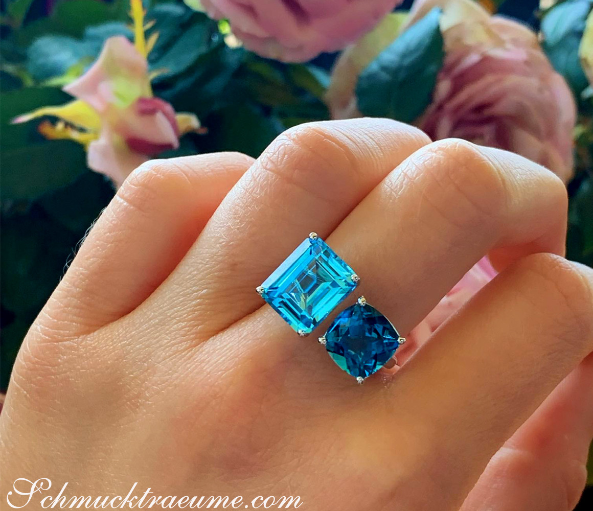 Blautopas-Ring mit quadratischen Steinen in Weißgold, Detailaufnahme, vor Rosenblüten.