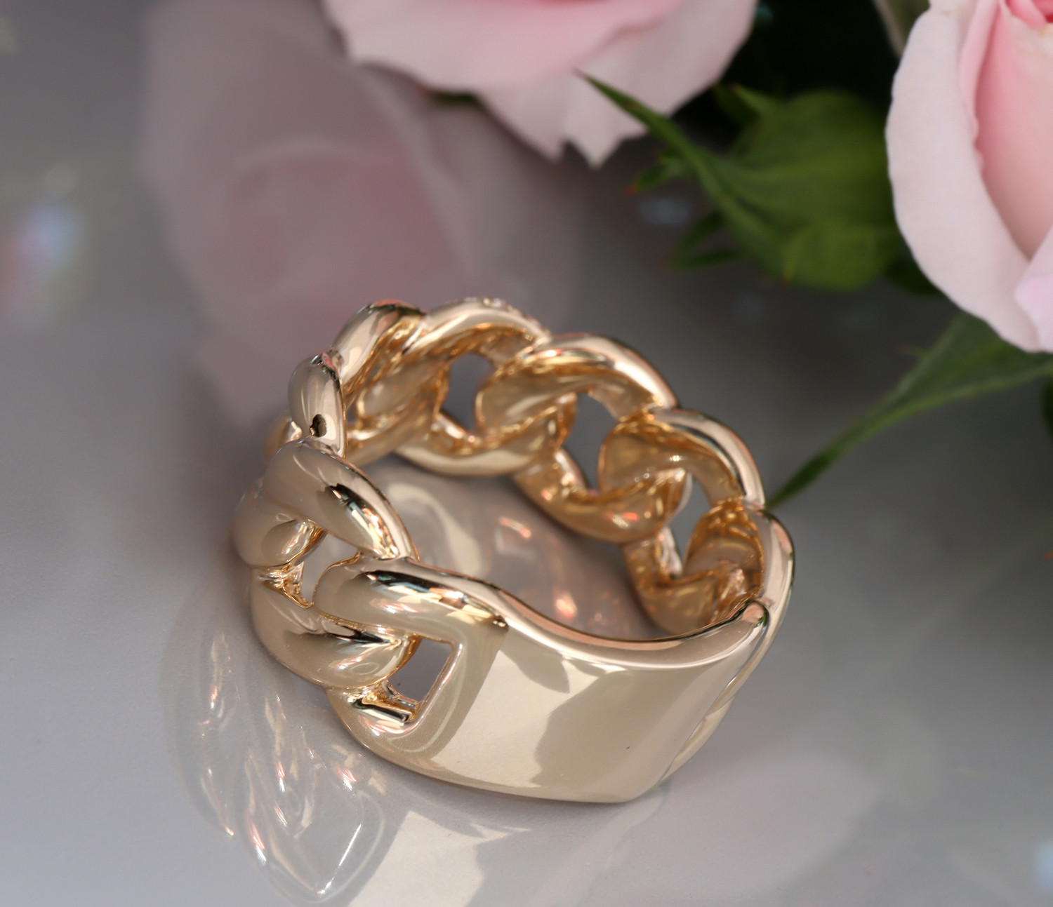 Goldener Panzerketterring mit Brillanten, Detailaufnahme, roséfarbenes Blumenhintergrund.