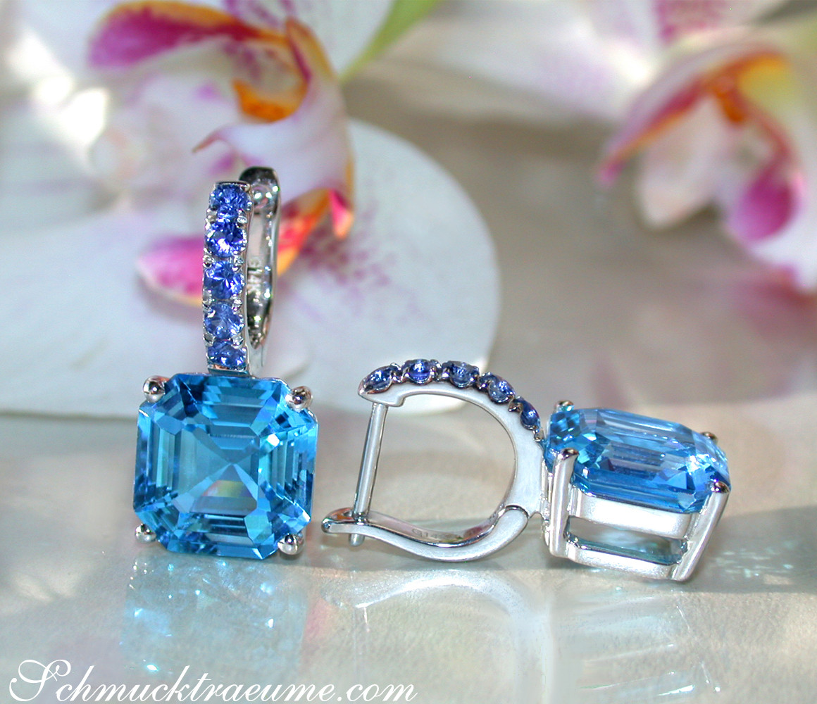 Blautopas-Ohrringe mit Saphiren in Weißgold, Detailaufnahme mit Orchideenblüte im Hintergrund