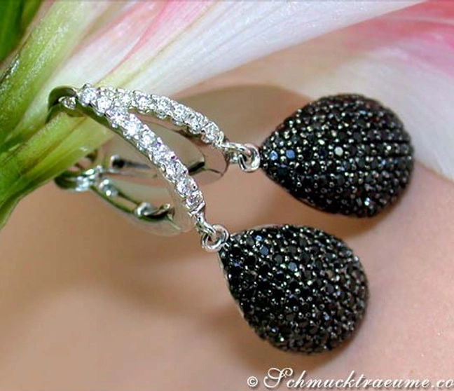 Schwarze Diamant-Ohrhänger mit weißen Diamantrand, getragen auf Hand. Schwarze Diamant-Ohrhänger mit weißen Diamantrand, getragen auf Hand.