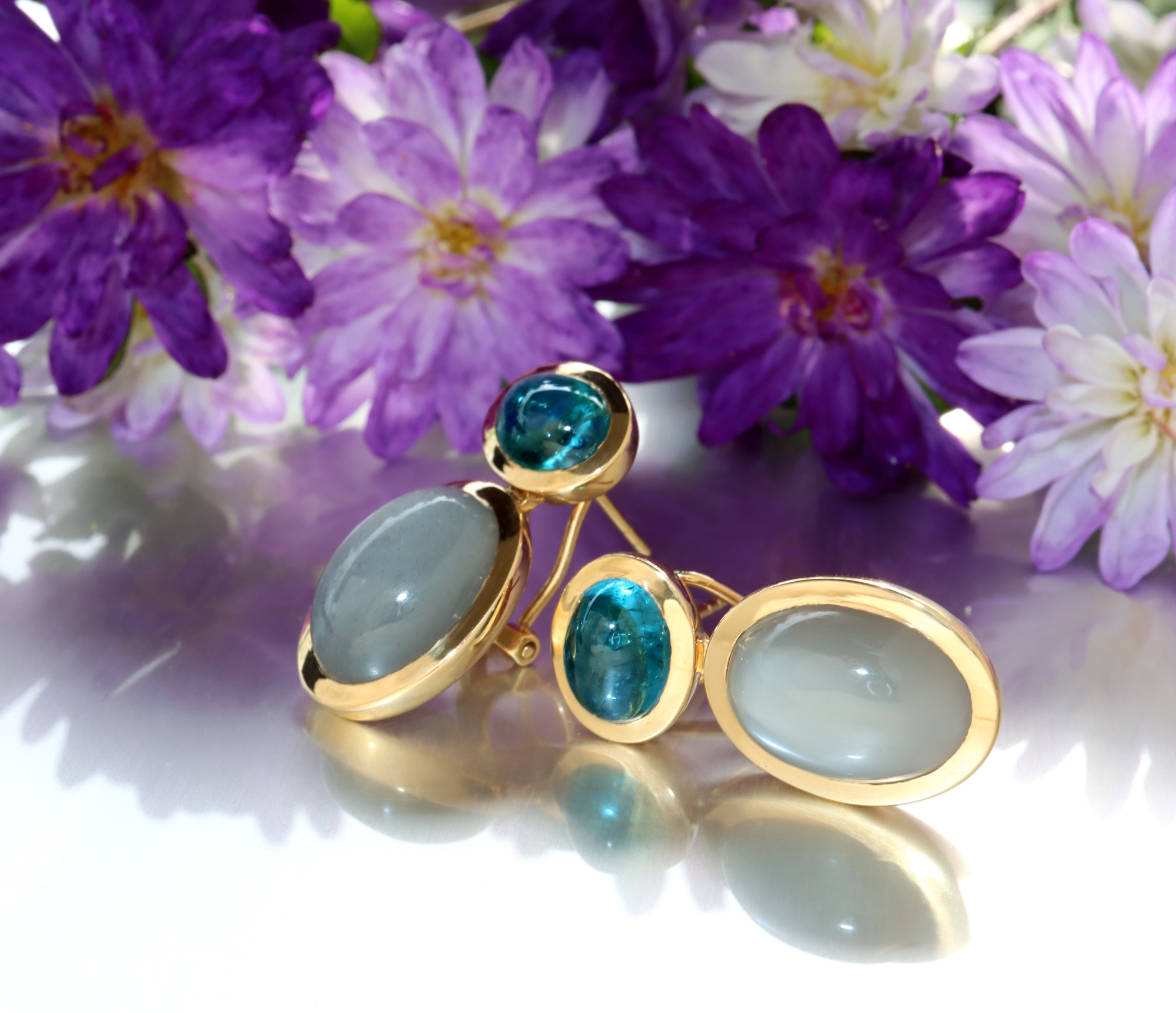 Goldene Ohrringe mit Mondsteinen und Blumen im Hintergrund