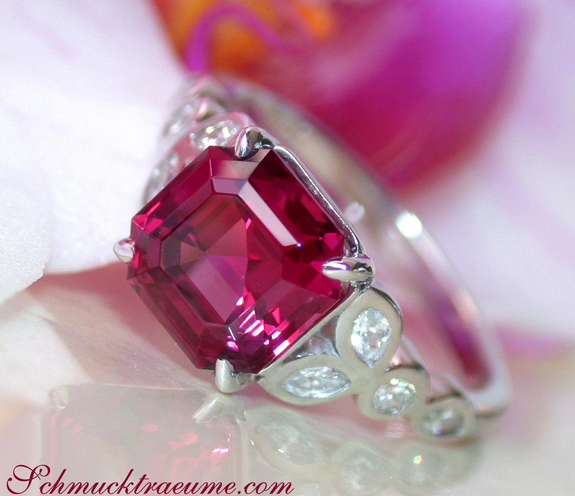 Weißgold-Ring mit Rhodolith und Diamanten, detailreich, Perspektive von oben, blütenähnlicher Hintergrund.