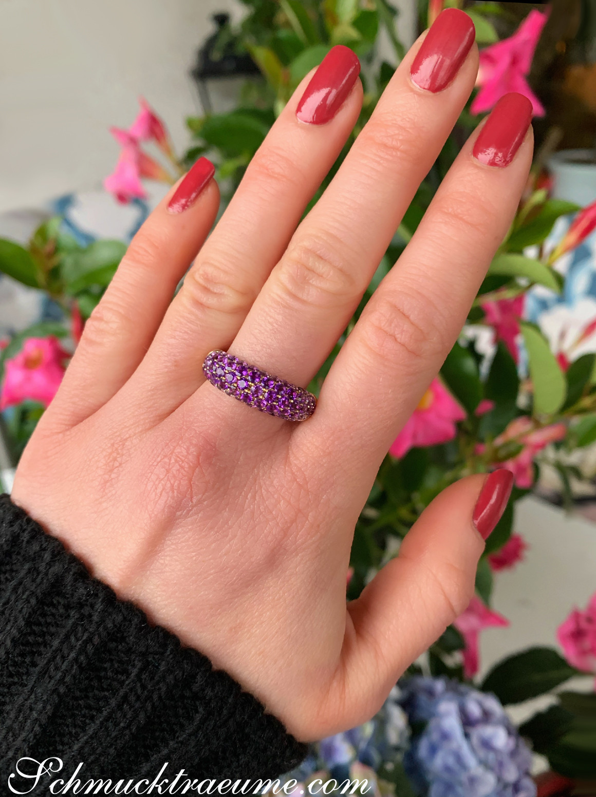 Amethyst Pavé Ring auf handgestreckter Hand vor Blumen
