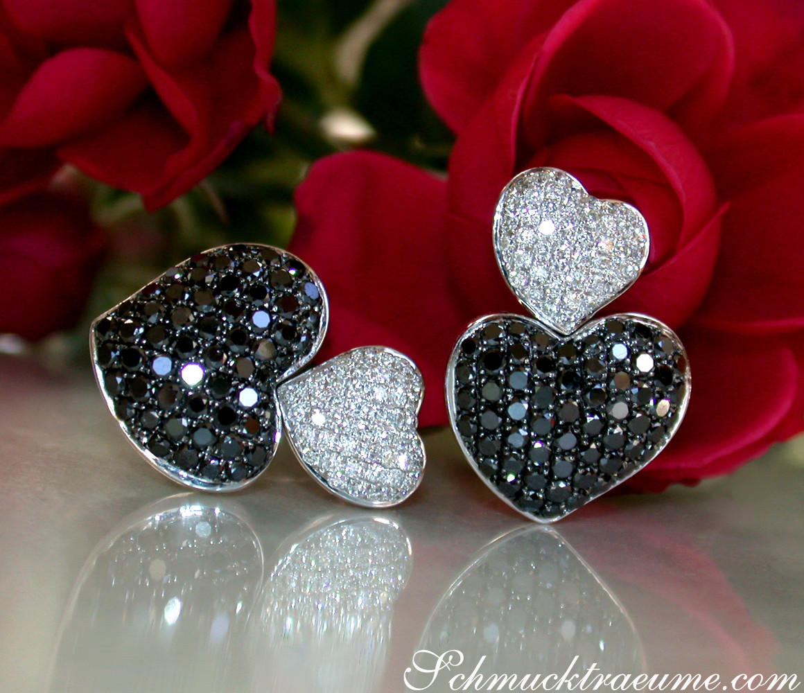 Herzohrringe mit schwarzen und weißen Diamanten, Detailaufnahme, Rosen im Hintergrund