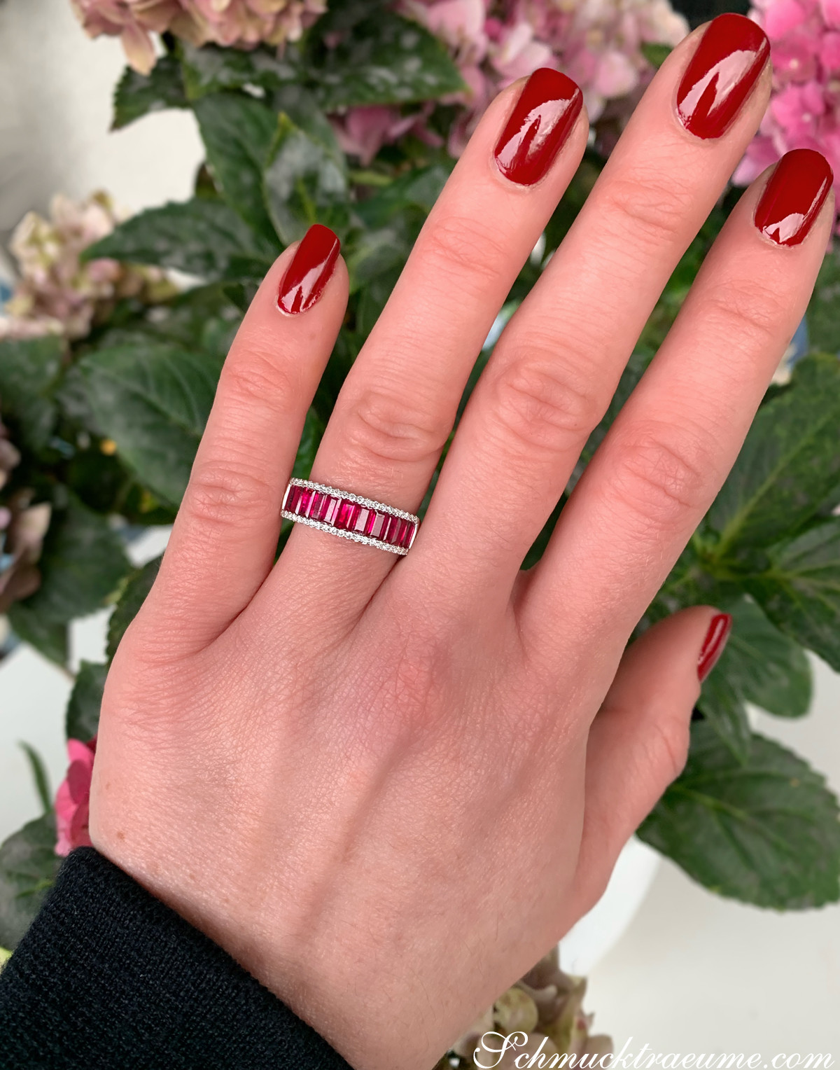 Ringszene mit roten Rubinen im Baguette-Schliff, Nagelkunst, Blumenhintergrund