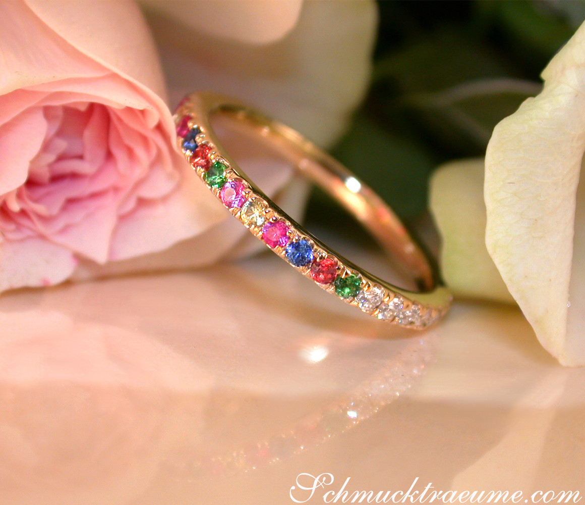 Goldener Ring mit Brillanten und Multicolor Saphiren, Detailaufnahme, Rosenblüten im Hintergrund.