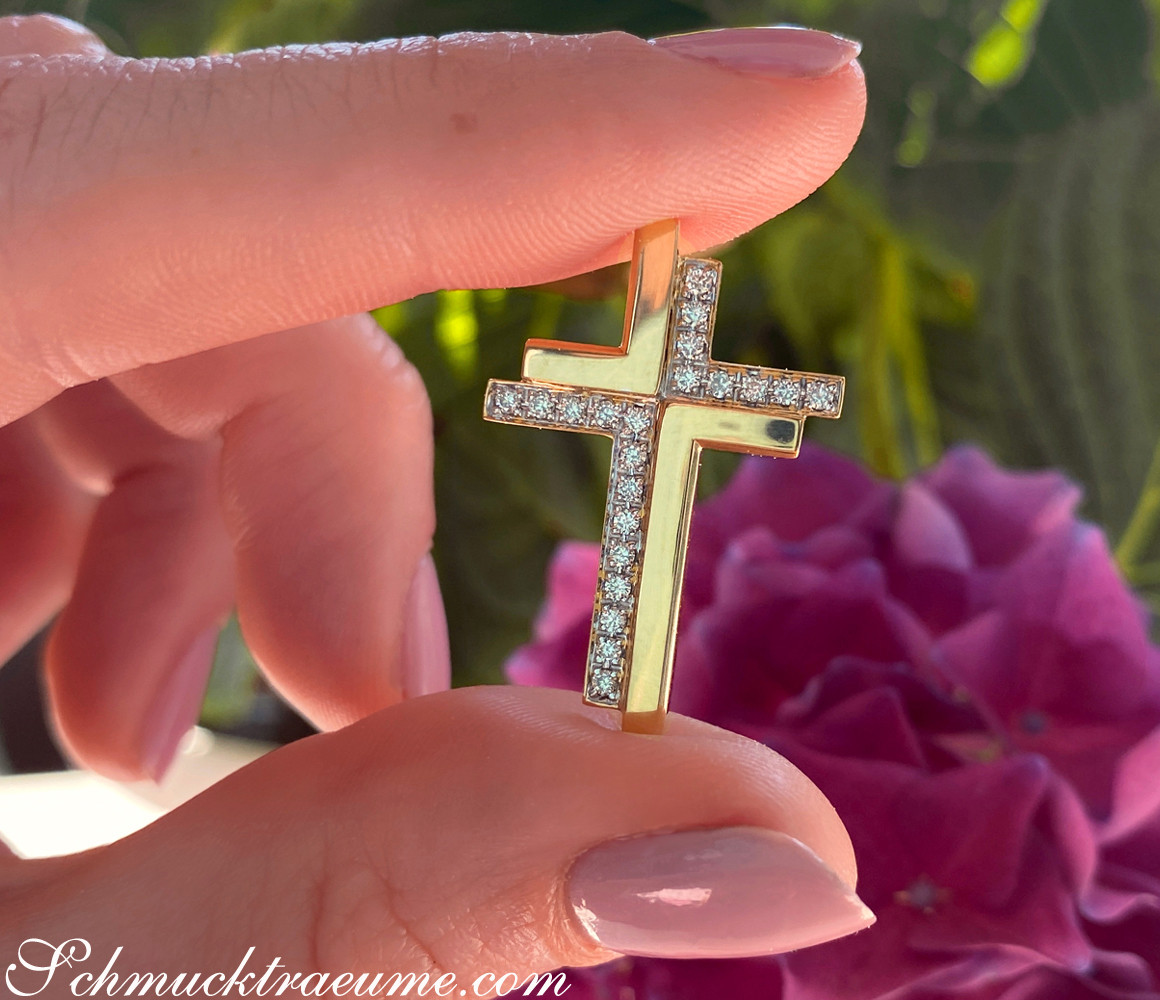 Goldener Kreuzanhänger „Duett“ mit Diamanten, Detailaufnahme, Hintergrund mit Blüte.