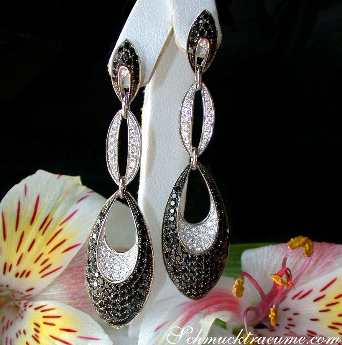 Schwarze & weiße Diamant-Ohrringe in Weißgold, elegant, modern, auf Blume präsentiert.