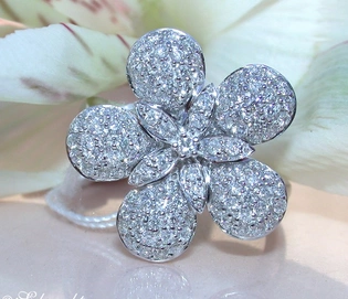 Blumenförmiger Brillantenring aus Weißgold 585, detailreich mit Diamanten verziert, vor Blütenblättern.