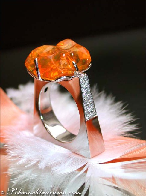 Futuristischer Feueropal-Ring mit Brillanten, Detailaufnahme, moderner Silhouette, Feder im Hintergrund.