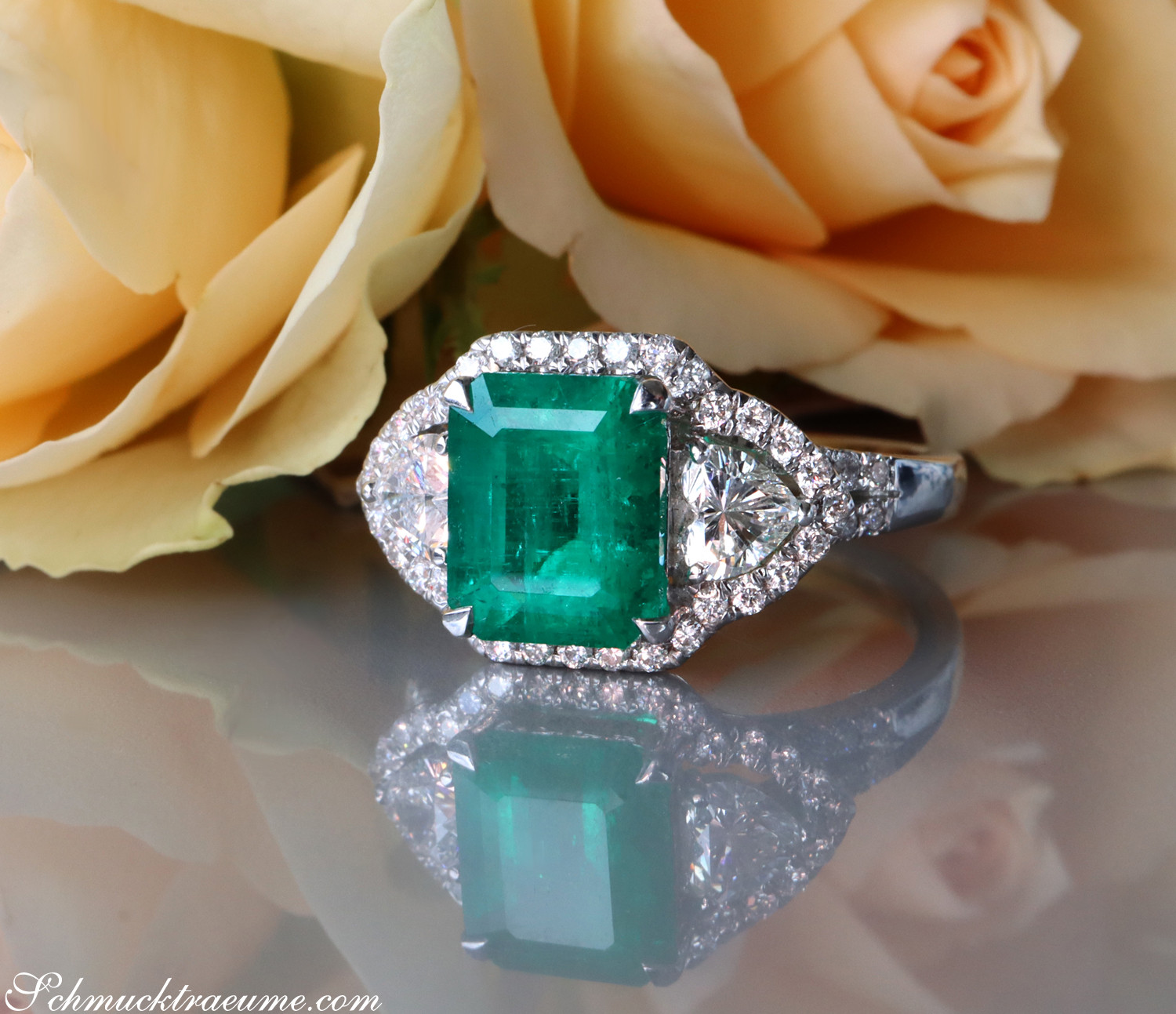 Verlobungsring mit kolumbianischem Smaragd und Diamant Herz, Detailaufnahme, Rosen im Hintergrund.