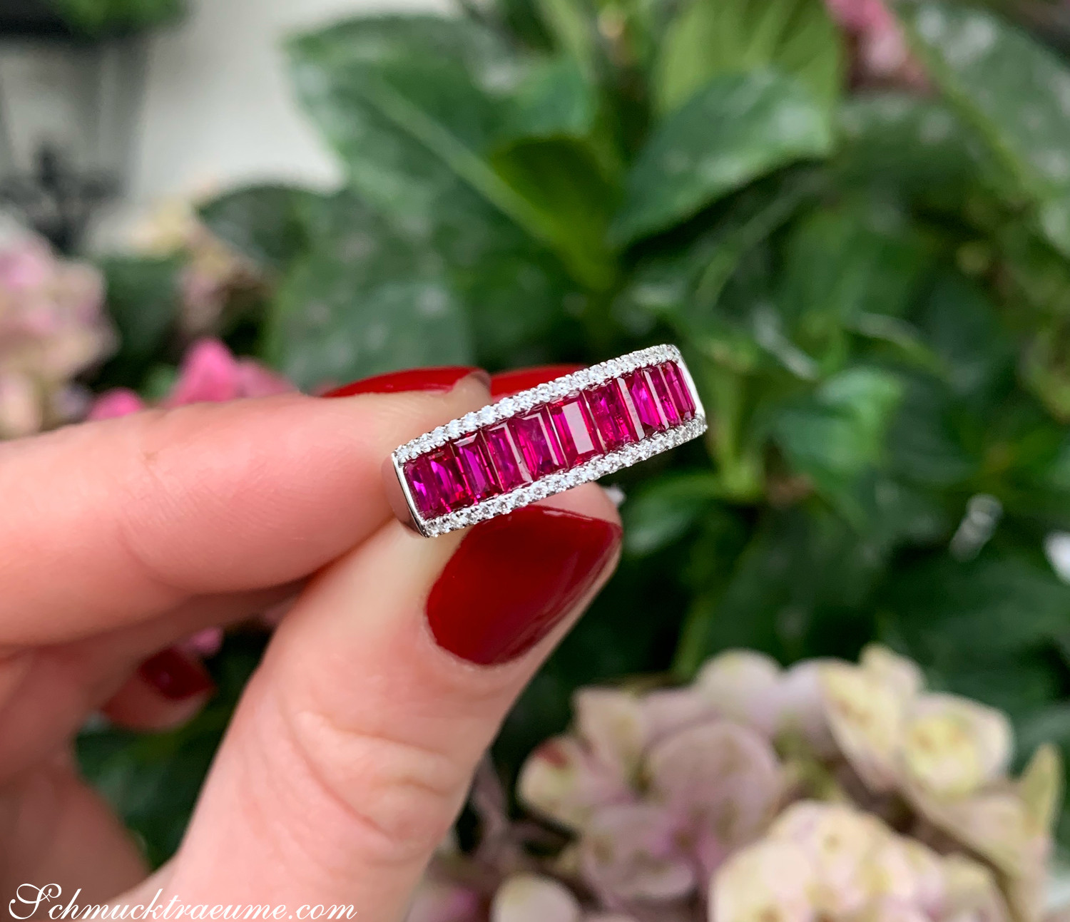 Rubin Baguette Ring mit Diamanten auf Fingern vor grüner Pflanze