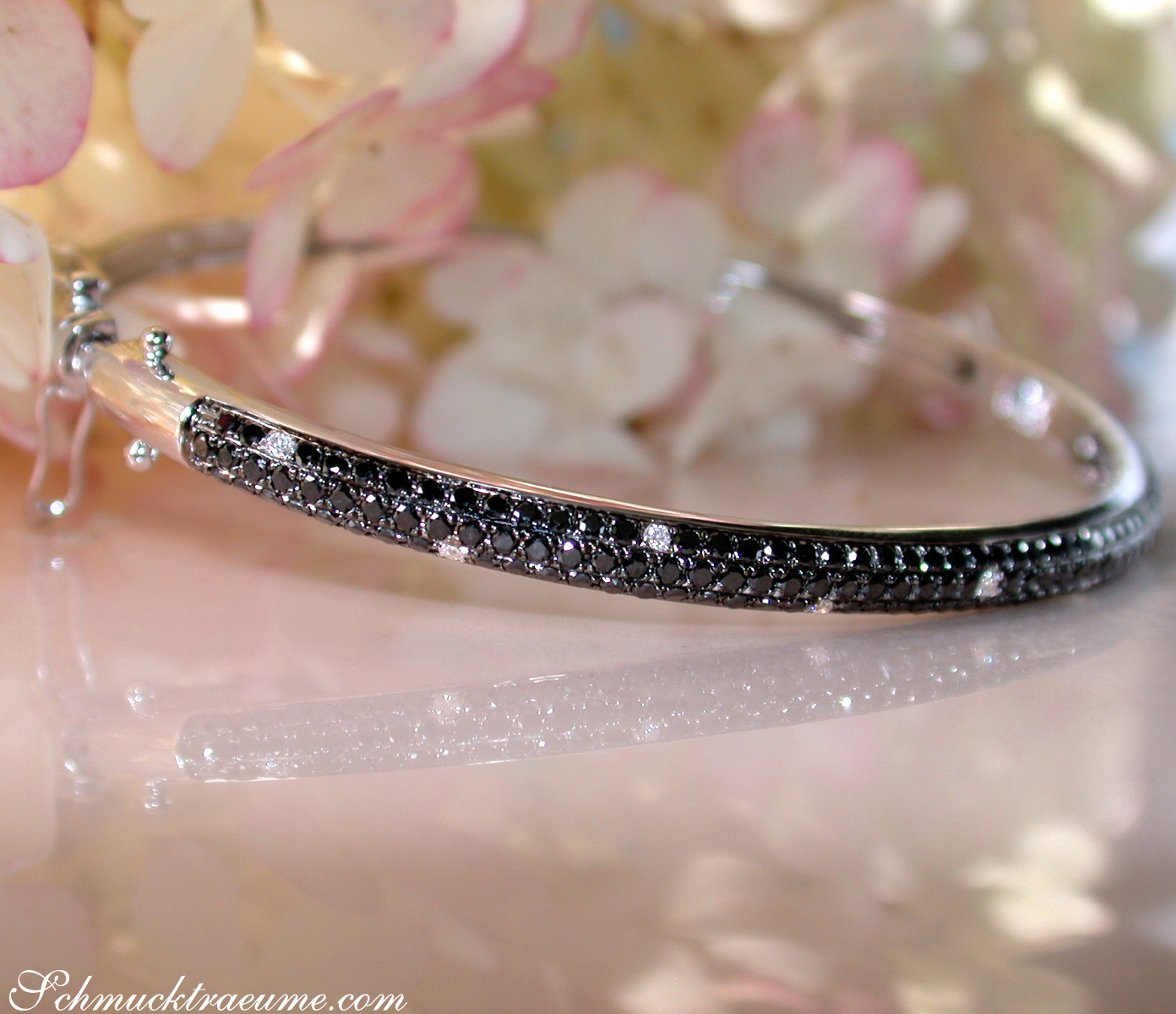 Schwarzdiamant-Armreif in Weißgold, Detailaufnahme, zarte Blüten im Hintergrund