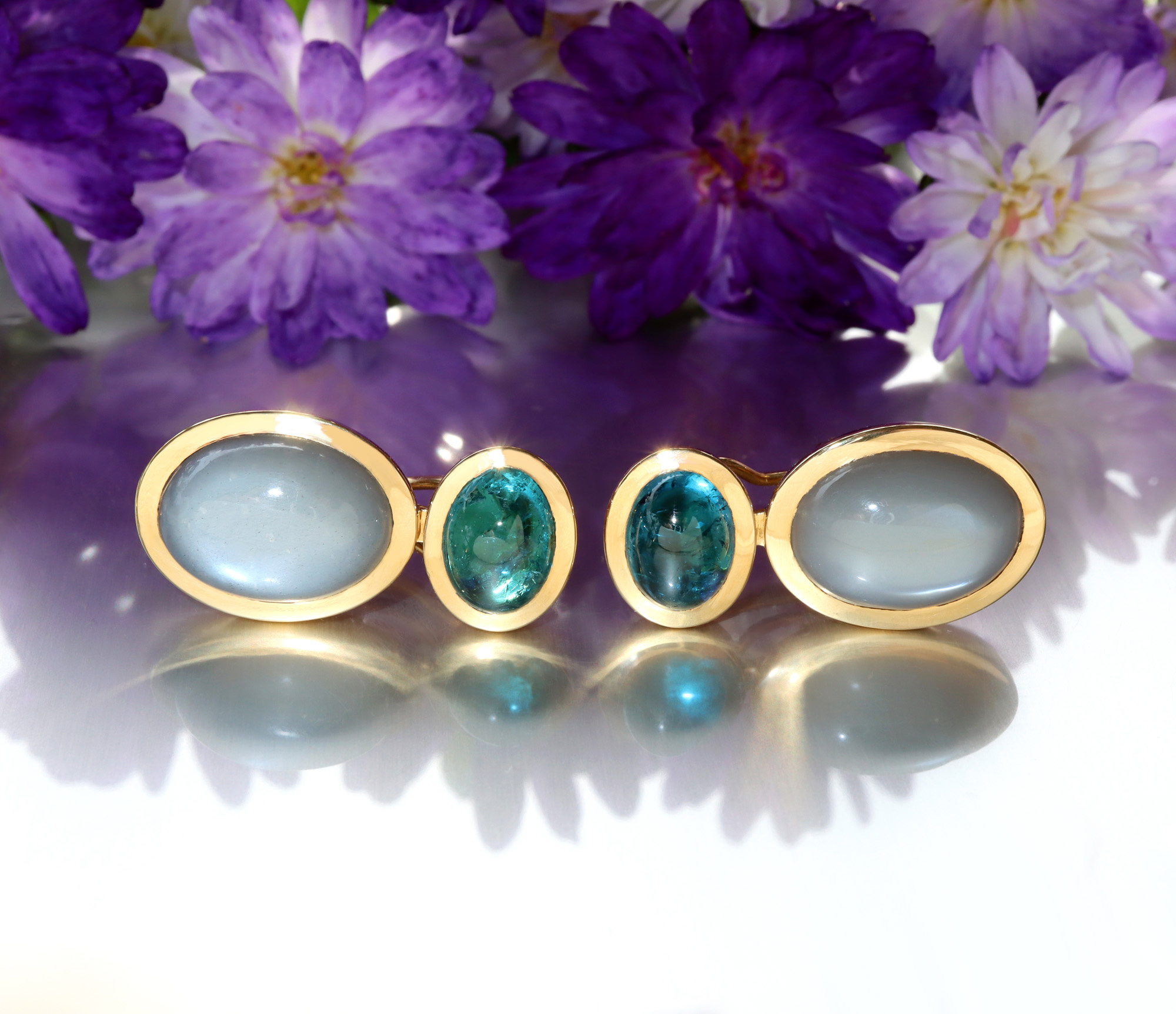 Goldene Ohrringe mit Mondsteinen und Blumen im Hintergrund