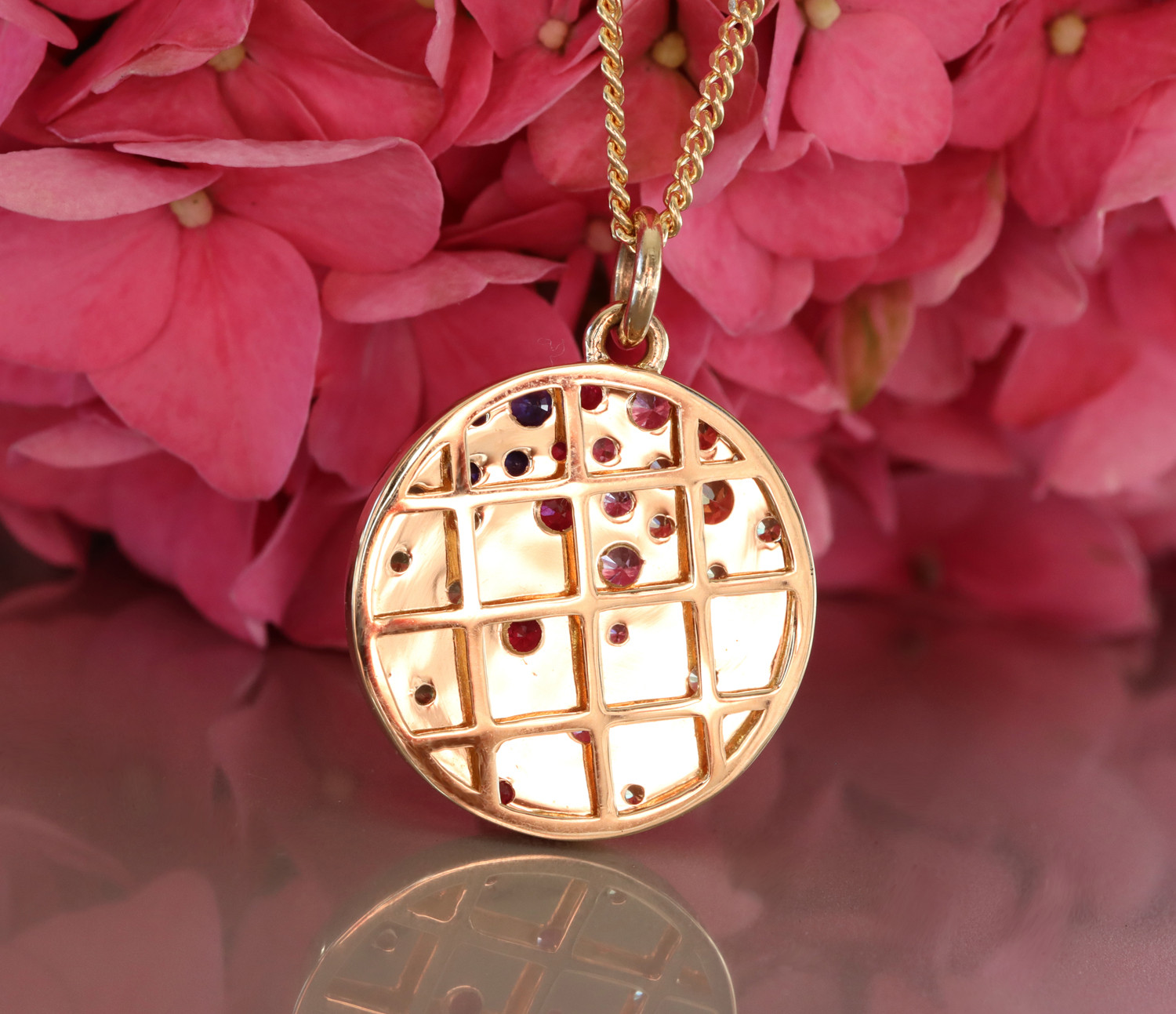 Goldene Medaillon-Halskette mit Saphiren und Rubinen auf rosa Blütenhintergrund