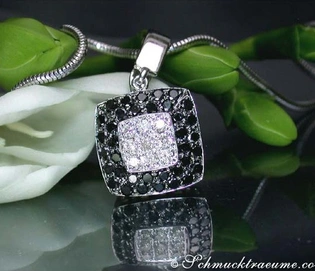 Silberner Carré-Anhänger mit schwarzen und weißen Diamanten, Detailaufnahme, vor grünem Blattwerk.