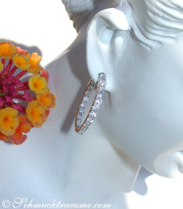 Weißgold-Brillanten-Creolen, Detailaufnahme, modelliert auf Kopfstein, Blumen im Hintergrund