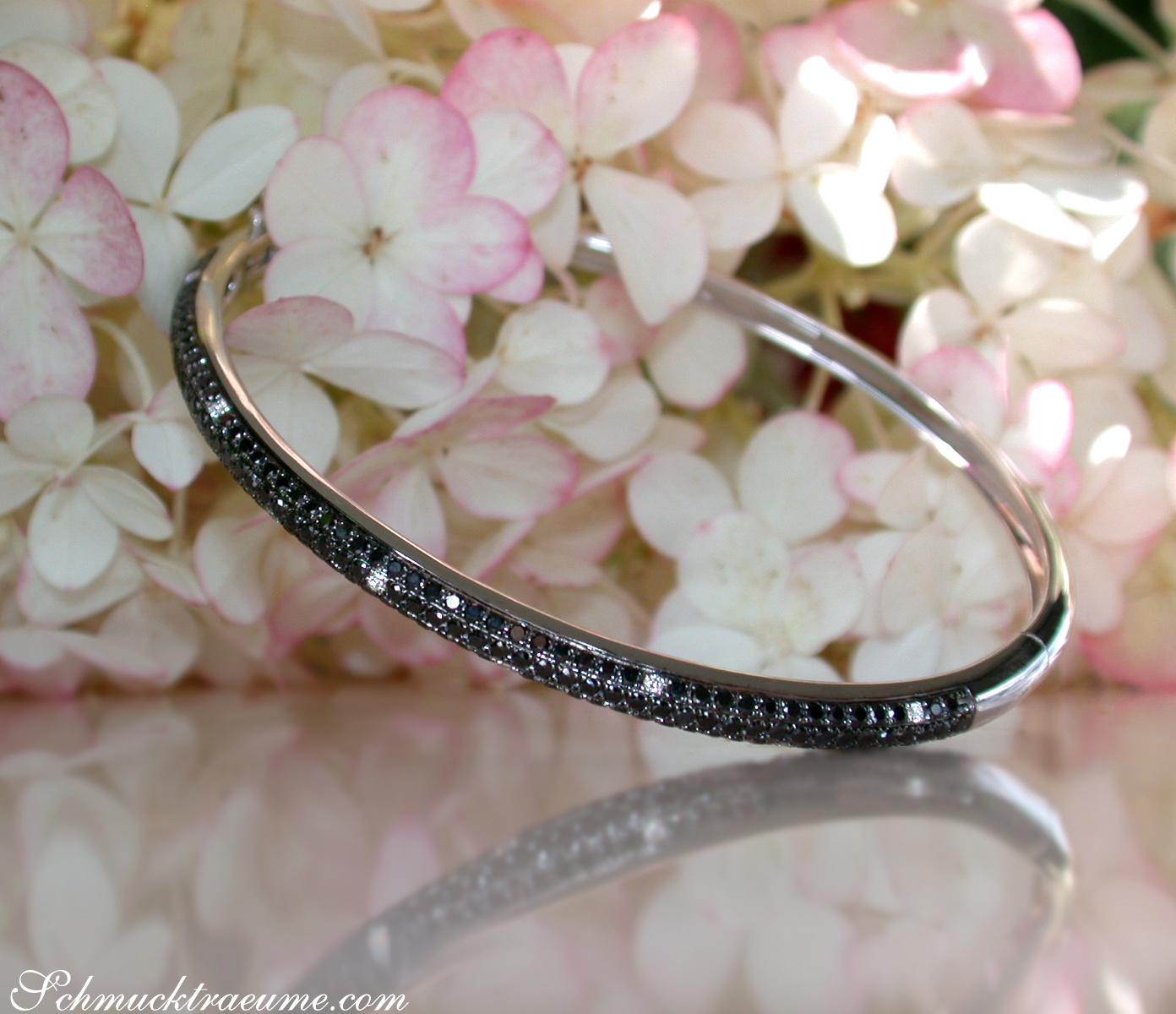 Silberner Armreif mit schwarzen Diamanten auf Hortensienblüten.