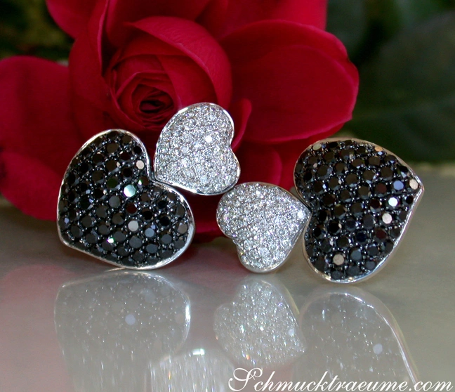 Herzformige Ohrstecker mit schwarzen und weißen Diamanten, vor Rosenblüte. Herzformige Ohrstecker mit schwarzen und weißen Diamanten, vor Rosenblüte.