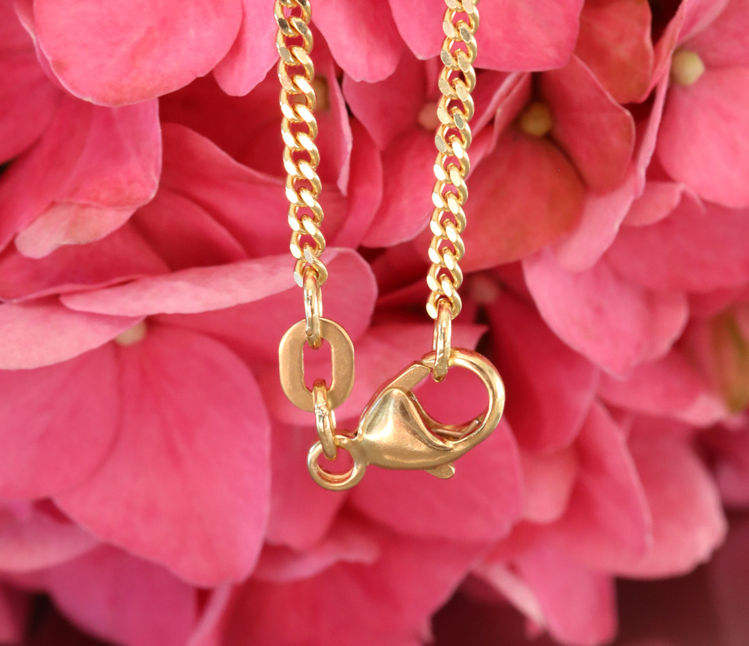 Goldkette mit Karabinerverschluss vor rosa Hortensienblüten