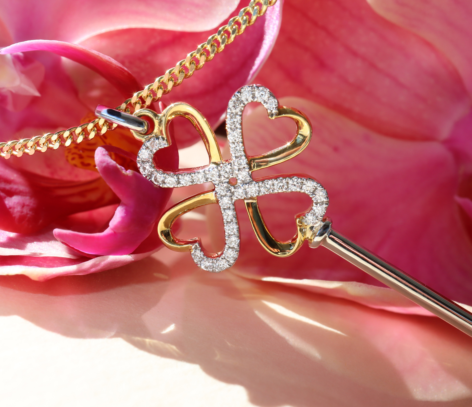 Goldener Schlüssel-Anhänger mit Diamanten, Detailaufnahme, vor rosa Blüte.