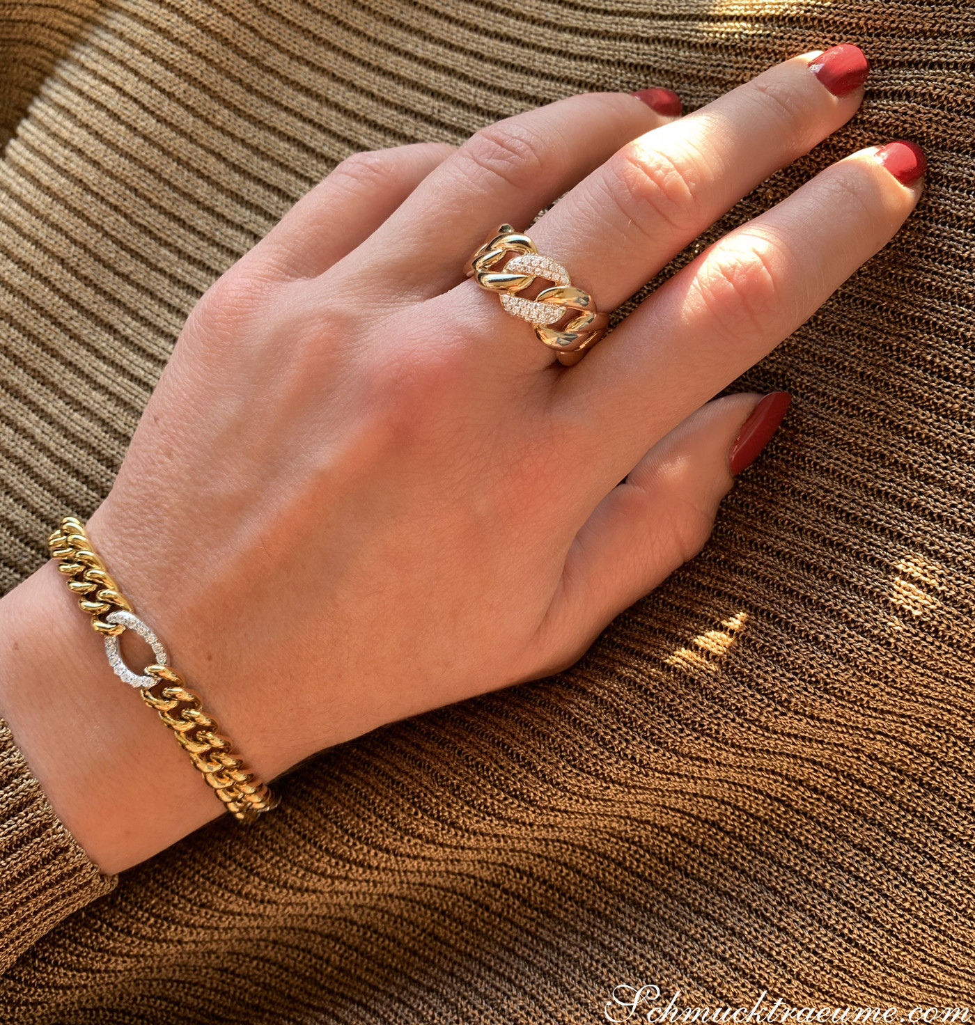 Goldenes Panzerarmband mit Brillanten, rote Nagelkunst, Hand auf gestreiftem Stoff.