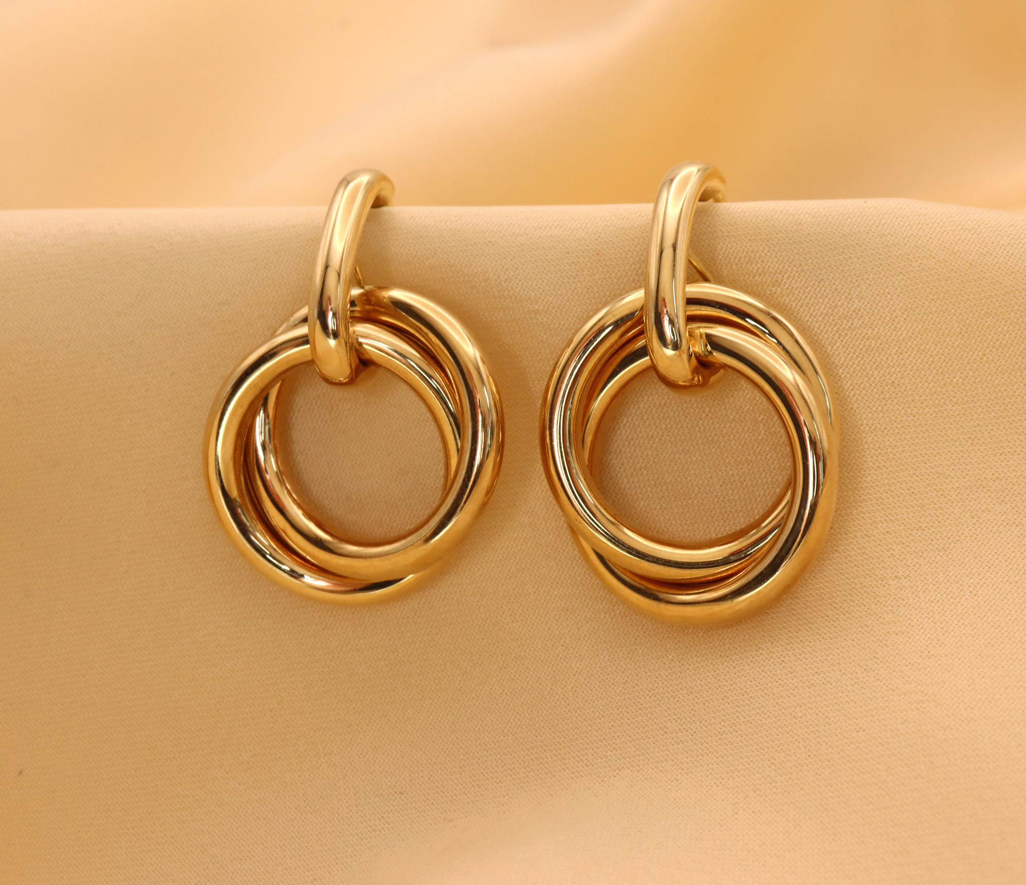 Goldene Ohrringe mit verschränkten Ringen auf cremefarbenem Hintergrund