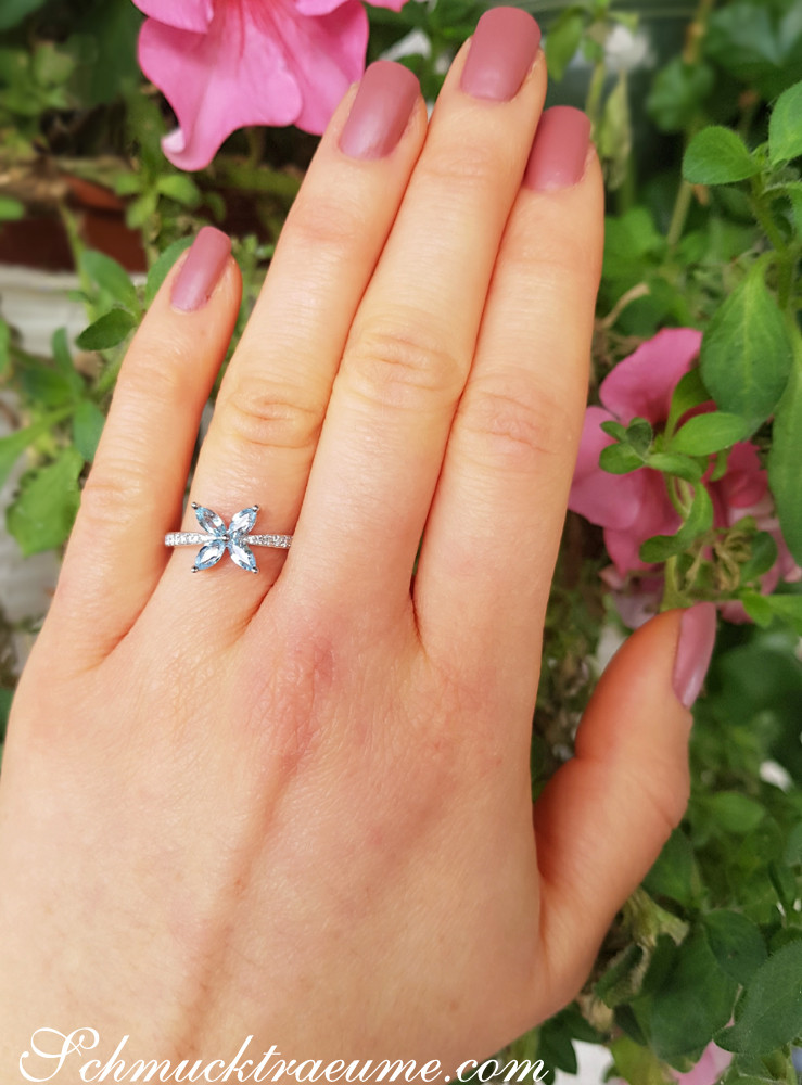 Blütenmotivierter Aquamarin-Ring mit Diamanten, detailreich, im Weißgold 585, vor grünen Pflanzen.