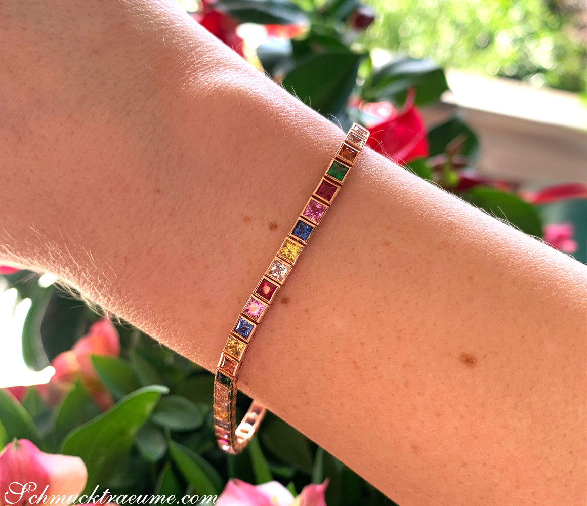 Prachtvolles Armband mit farbenfrohen Steinen auf Hand vor Blumen.