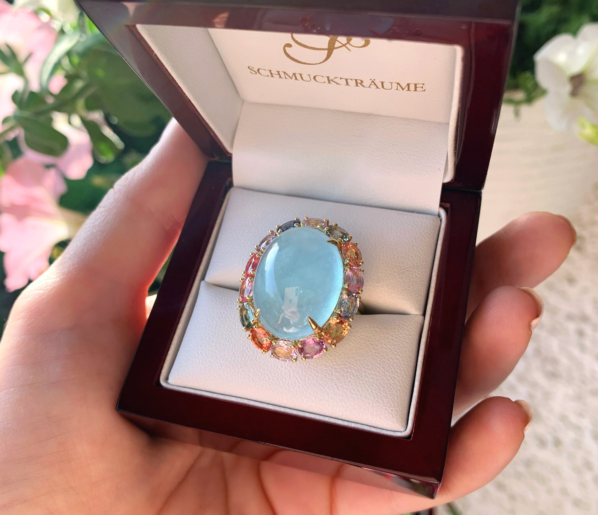 Hand mit Opulenter Milky Aquamarin Ring mit Multicolor Saphiren in Goldschmuckschachtel