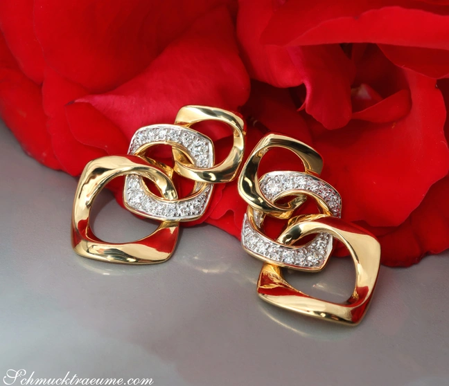 Goldene Ohrringe mit Brillanten im Gliederdesign vor rotem Rosenblatt Goldene Ohrringe mit Brillanten im Gliederdesign vor rotem Rosenblatt