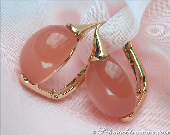 Goldene Ohrringe mit rosa Mondsteinen auf weißem Stoff.