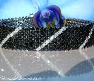 Schwarz-weißes Diamant-Armband mit Glanz und Glitter, blauer Orchidee im Hintergrund.