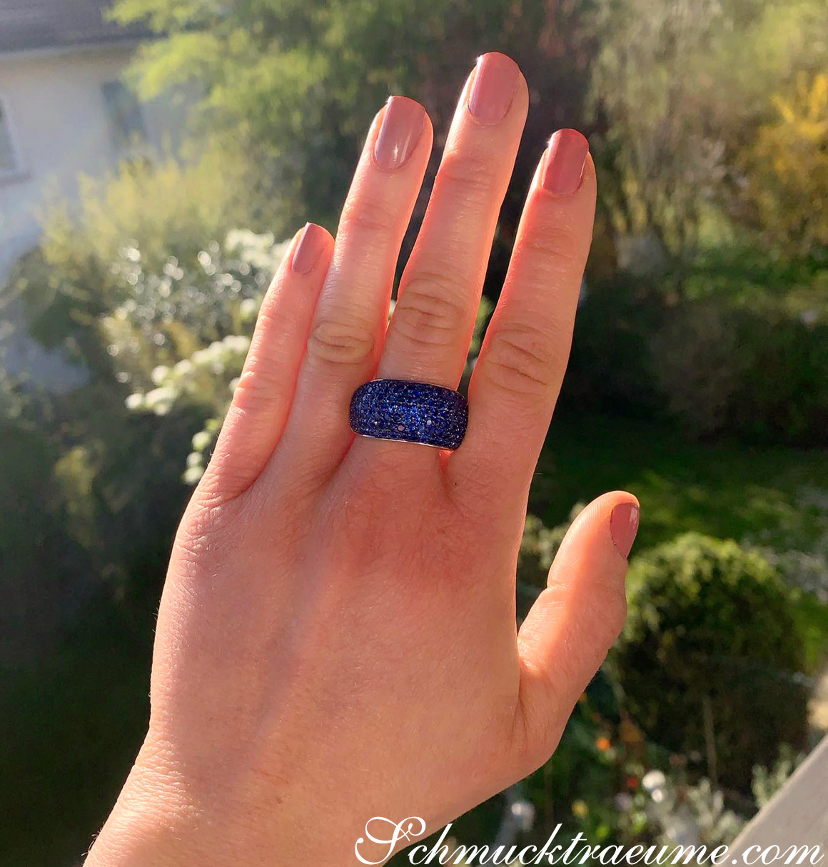 Hand mit blauem Saphir-Pavé-Ring im Sonnenlicht