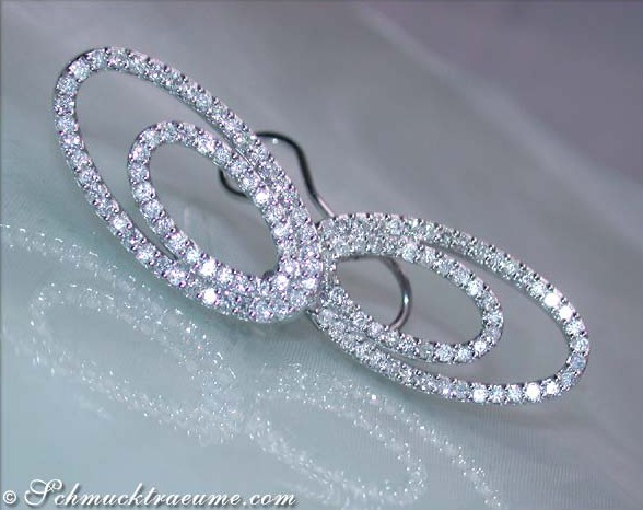 Weißgold-Ohrringe mit Brillanten in Ellipsenform, detailreich, auf weißem Tuch liegend.