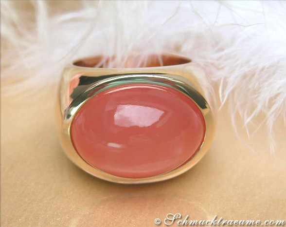 Goldener Mondstein-Ring mit ovaler Steinverzierung, auf Federhintergrund liegend.