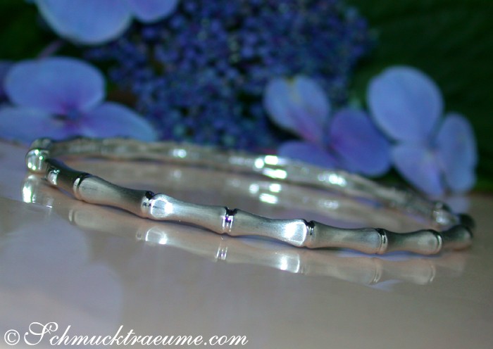 Satiniertes Weißgold Bambus-Armreif mit Diamanten, Detailaufnahme auf glänzender Oberfläche, blühende Hortensien im