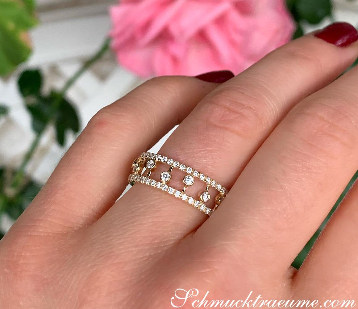 Goldener Diamantenring mit TW SI, 0.950 Karat, auf Handfinger mit rosa Blume im Hintergrund.