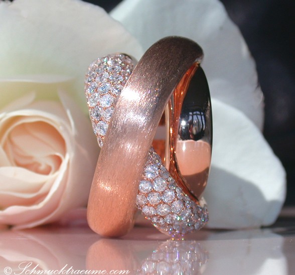 Roségold-Ring mit feinen Brillanten, überkreuzt, vor Rosenblüte