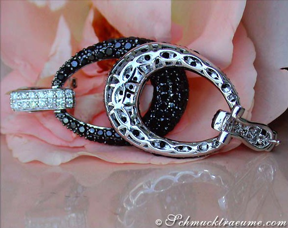 Schwarze Diamant-Ohrringe, Detailaufnahme, weißgoldene Rahmen, rosafarbene Blüte im Hintergrund