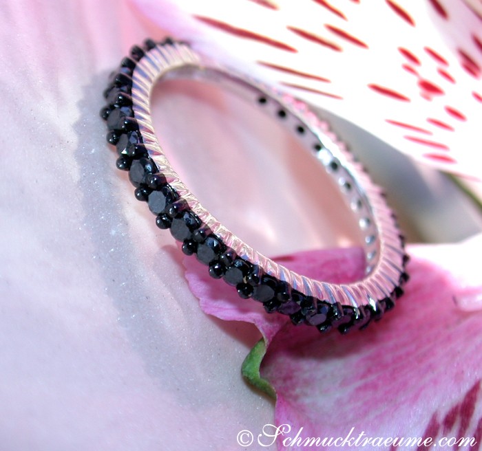 Schwarzdiamant-Memory-Ring aus Weißgold 750, Detailaufnahme mit feinen Strukturlinien, auf rosa Blütenblatt gelegt