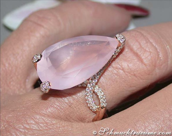 Rosenquarz-Tropfen-Ring mit Brillanten auf Handfinger, detailreich, warmes Licht