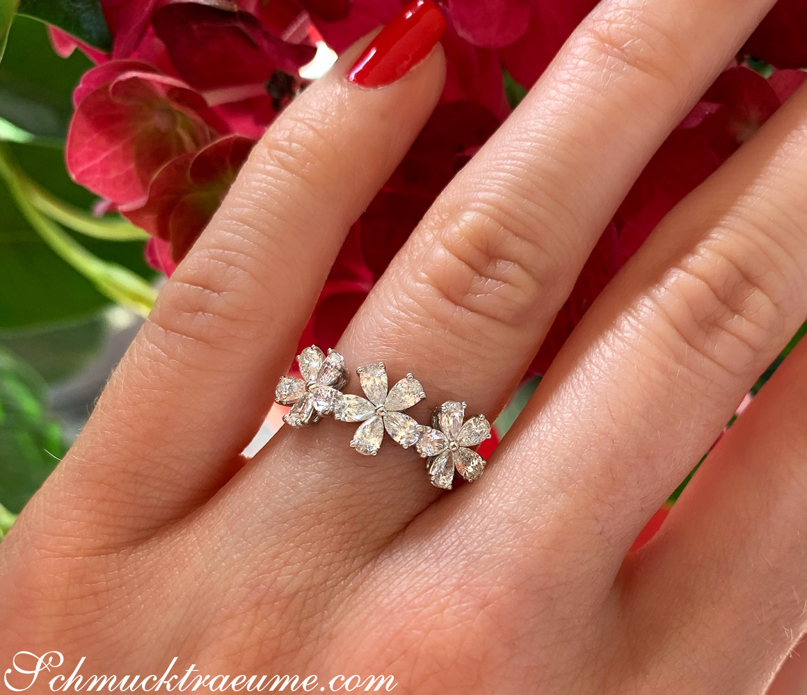 Femininer Diamantenblüten-Ring auf Hand vor roten Blüten.