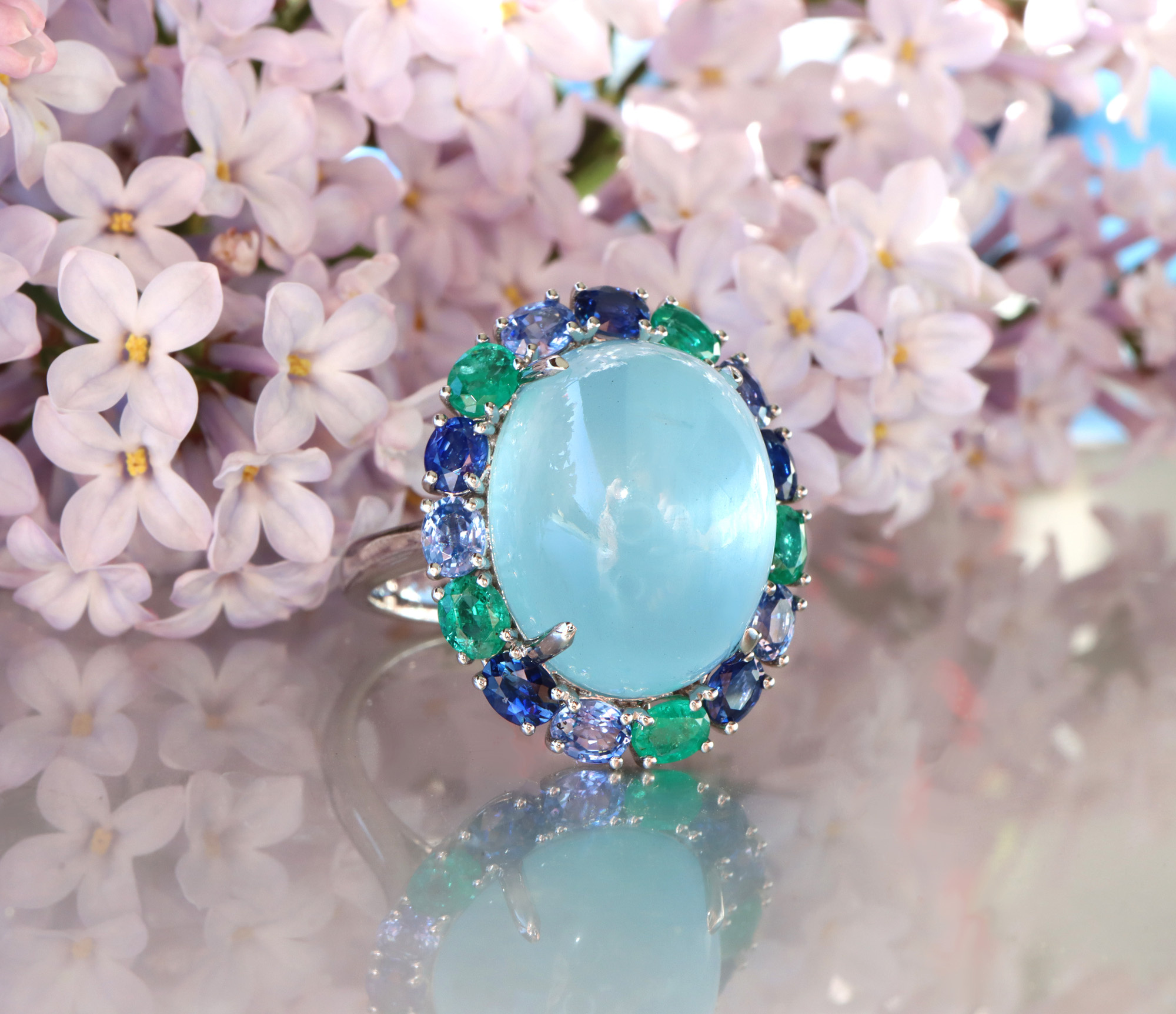 Milky Aquamarin-Ring mit Saphiren und Smaragden auf Lilienblütenhintergrund